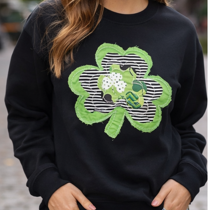 Black sweatshirt with a green shamrock design worn by a person.