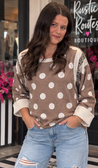 Front view of mocha oversized ivory polka dot top featuring leopard shoulder accents, a ribbed neckline and wide ivory cuffs with blue jeans.