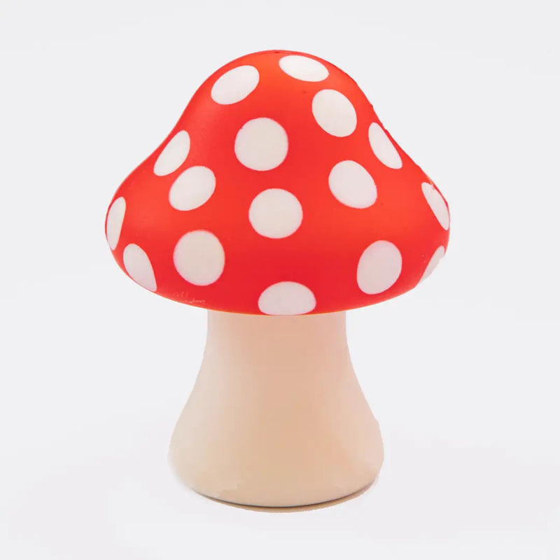 Soft red mushroom squishy with white polka dots and a cream-colored stem on a light background