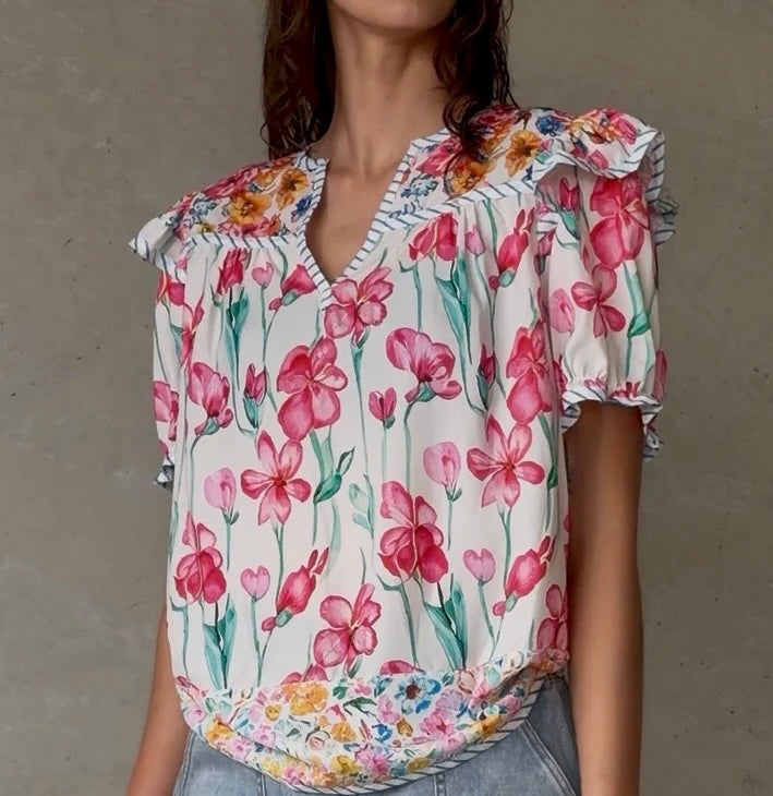 Brunette woman wearing floral ruffle sleeve blouse with denim shorts and wedge heels on white background
