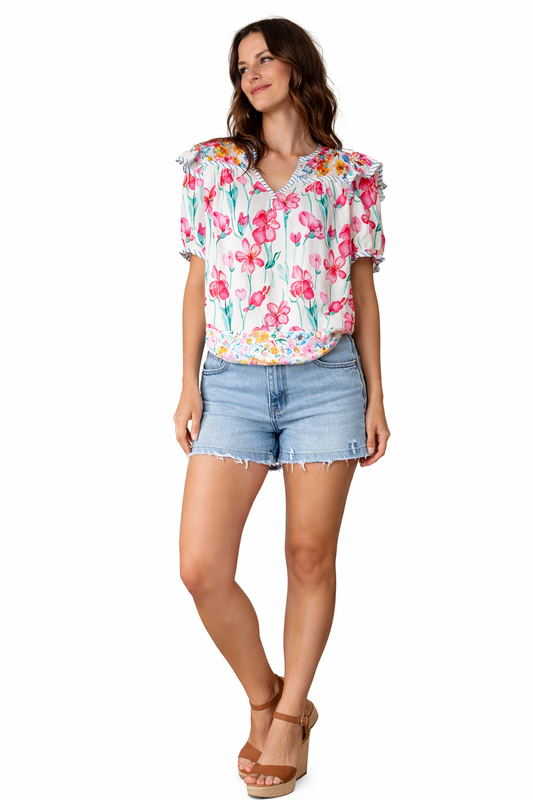 Brunette woman wearing floral ruffle sleeve blouse with denim shorts and wedge heels on white background