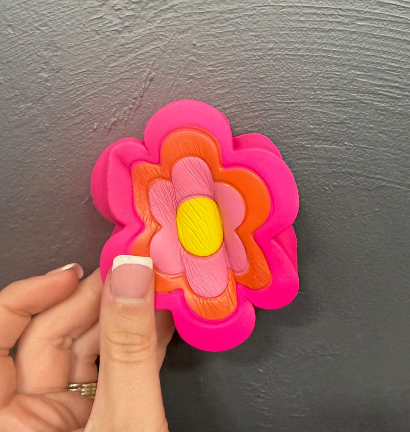 Colorful flower-shaped de-stress ball in pink, orange, light pink, and yellow held in a hand against a dark background