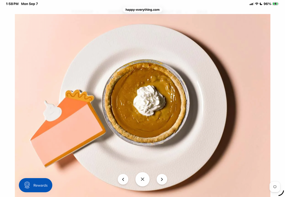 A top-down styled flat-lay of a pumpkin pie on a white plate with a dollop of whipped cream, alongside a paper cutout of a pie slice, set against a soft peach background.