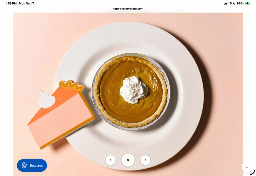 A top-down styled flat-lay of a pumpkin pie on a white plate with a dollop of whipped cream, alongside a paper cutout of a pie slice, set against a soft peach background.