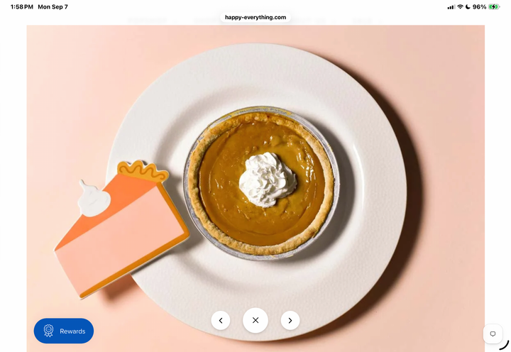 A top-down styled flat-lay of a pumpkin pie on a white plate with a dollop of whipped cream, alongside a paper cutout of a pie slice, set against a soft peach background.