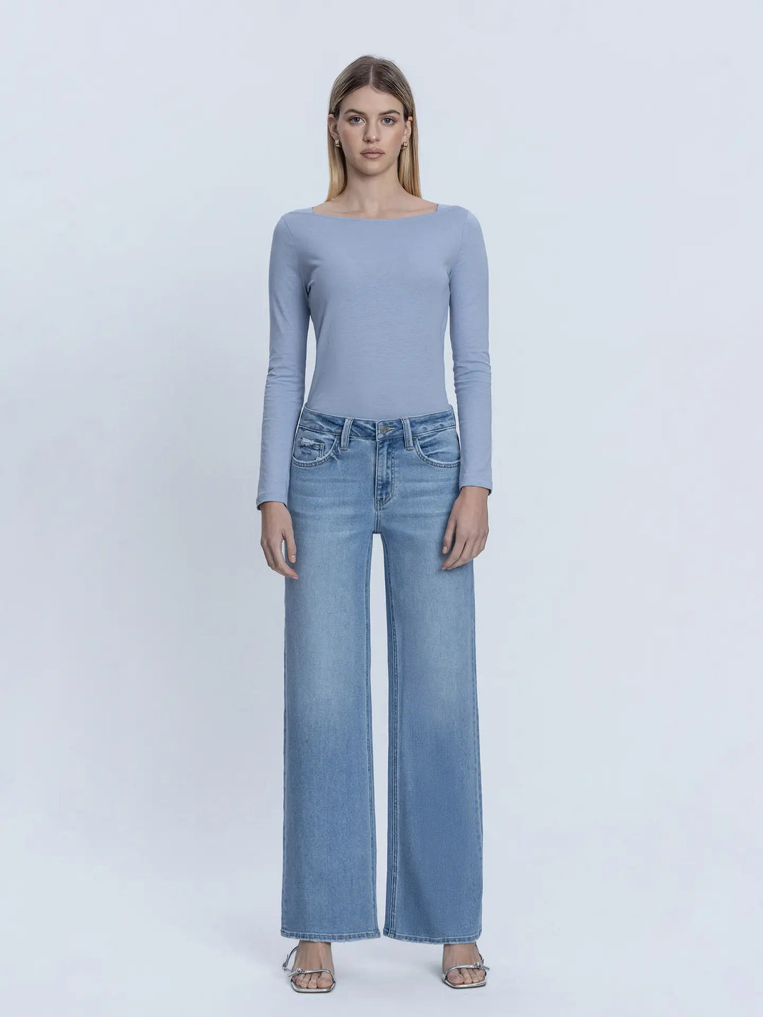 Woman wearing a light blue long-sleeve top and jeans on a white background